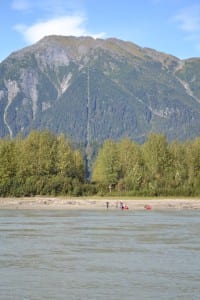 Kayakers rest near the U.S.-Canadian border on the Stikine River, marked by a line of cleared trees. (KFSK file photo)